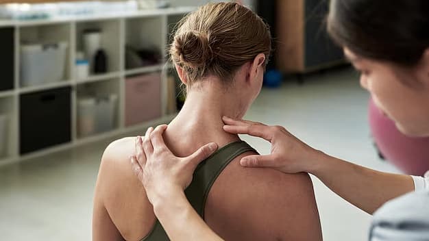 Fysiotherapeut onderzoekt de nek en schouders van een patiënt tijdens een behandeling
