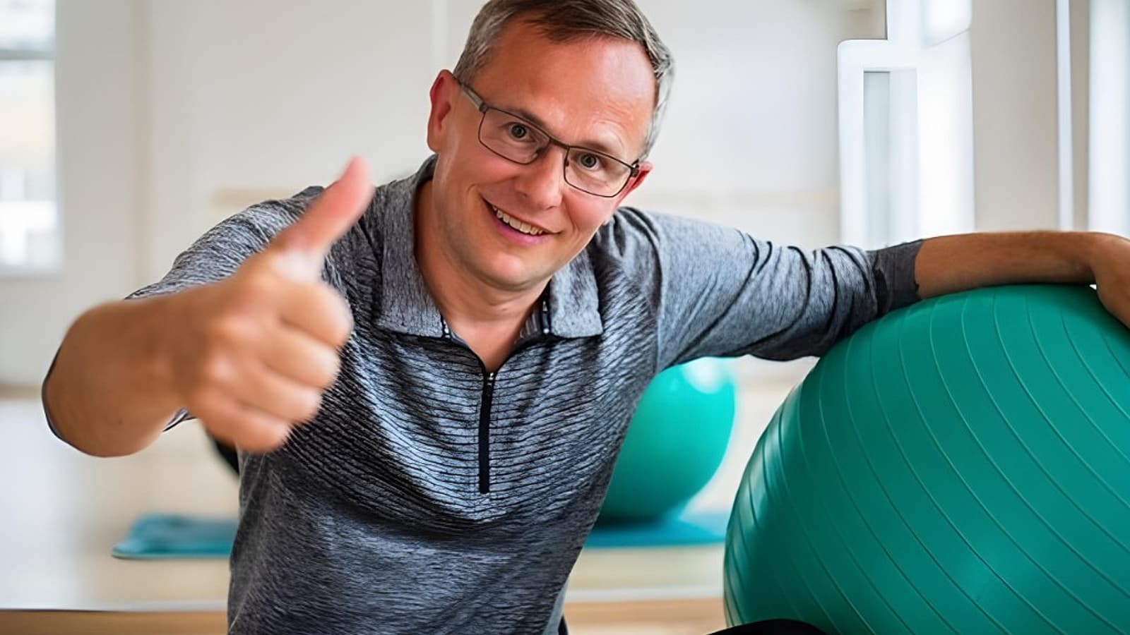 Glimlachende fysiotherapeut in de praktijk geeft een duim omhoog naast een oefenbal
